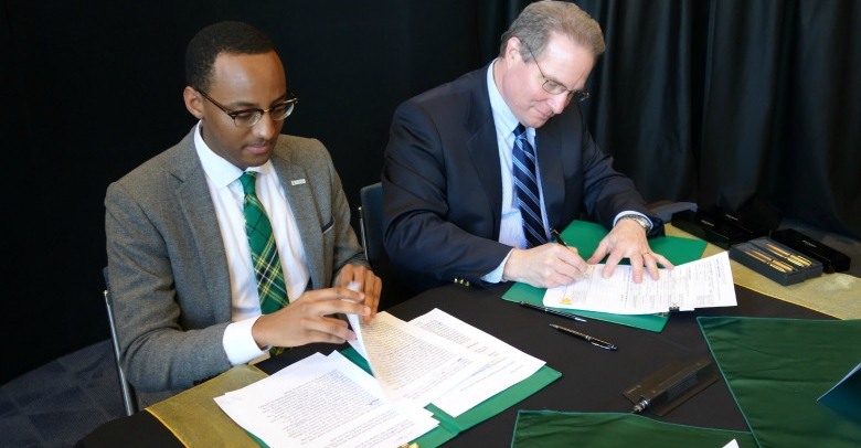 Provost Carl Amrhein and Students' Union president Petros Kusmu sign the approval of "Green and Gold Week," a new fall break for UAlberta students.